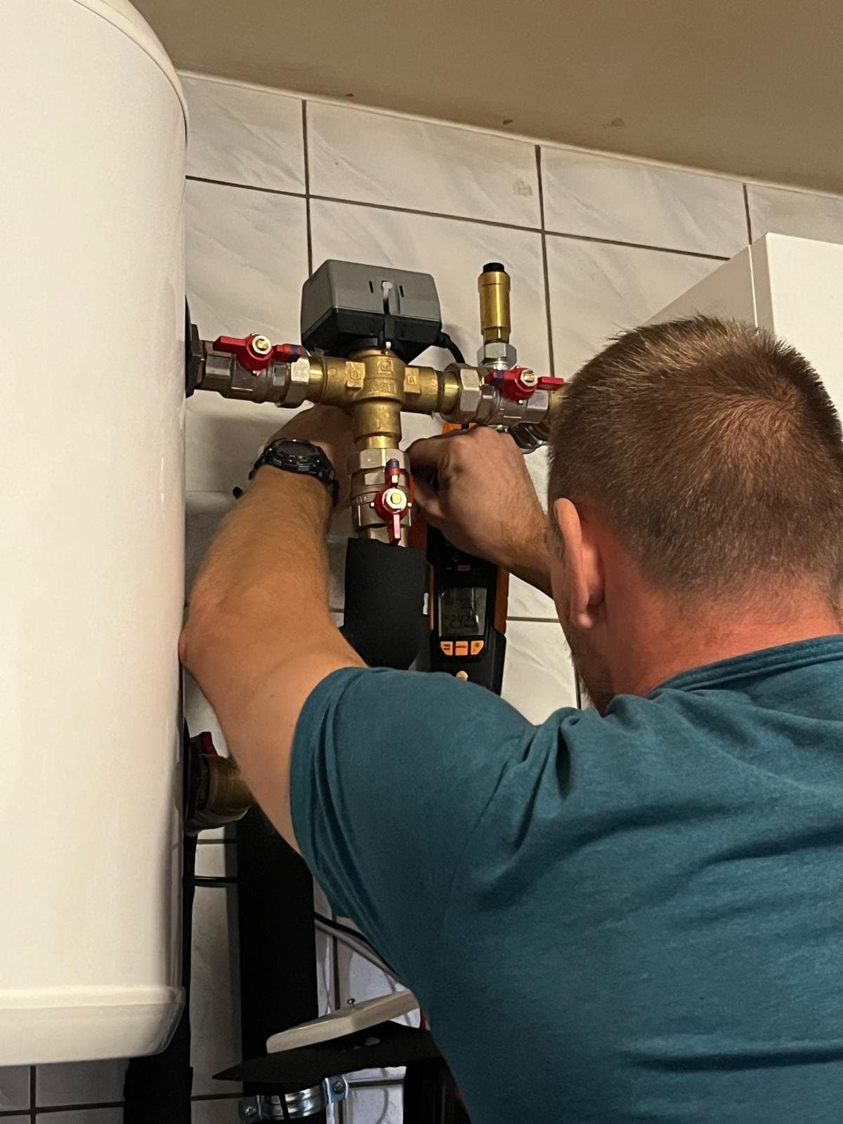 Robert Poczaj wykonuje pomiary miernikiem TESTO przy zaworach instalacji pompy ciepła Panasonic Aquarea